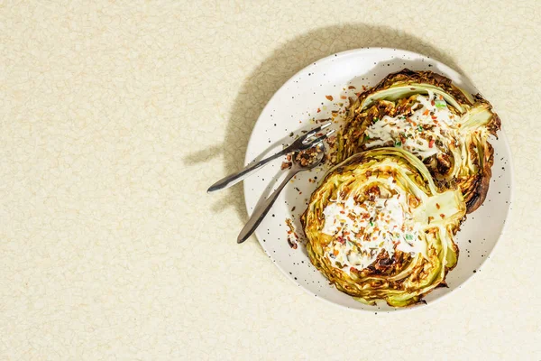 Ev yapımı vejetaryen lahana bifteği, baharat ve sos. Sağlıklı yiyecekler servis tabağında yemeye hazır, çatal bıçak takımı. Taş beton zemin, üst görünüm