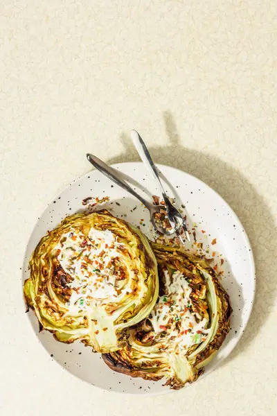 Ev yapımı vejetaryen lahana bifteği, baharat ve sos. Sağlıklı yiyecekler servis tabağında yemeye hazır, çatal bıçak takımı. Taş beton zemin, üst görünüm