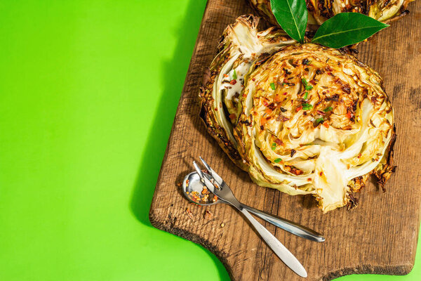 Homemade vegan cabbage steaks with herbs and spices. Healthy food ready to eat on a wooden cutting board. Modern hard light, dark shadow, bright green background, top view