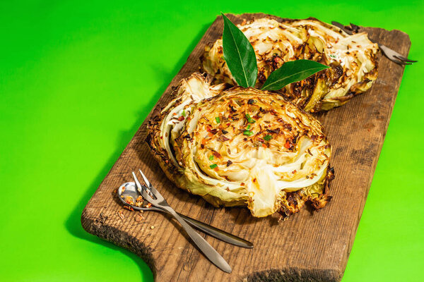 Homemade vegan cabbage steaks with herbs and spices. Healthy food ready to eat on a wooden cutting board. Modern hard light, dark shadow, bright green background, copy space