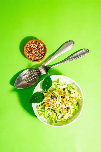 Bahar diyeti salatası. Taze vejetaryen vitamin yiyeceği. Dilimlenmiş lahana, baharat, zeytinyağı, kuru böğürtlen. Sağlıklı yaşam tarzı kavramı. Modaya uygun sert ışık, koyu gölge, parlak yeşil arkaplan, üst manzara