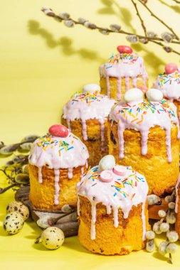 Geleneksel Paskalya pastası. Şekerleme ve dekorlu şenlikli tatlı yiyecekler. Yumurta, yuva, söğüt, modaya uygun sert ışık, karanlık gölge. Parlak sarı arka planda geleneksel pişirme, kapat