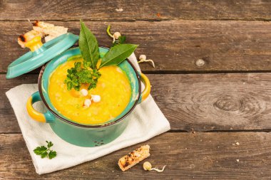 Eski ahşap arka planda bir kasede bezelye kremalı çorba. Kuru baklagiller, tost, kızarmış ekmekler ve yeşiller. Lezzetli vejetaryen sağlıklı yemek. Modaya uygun sert bir ışık, karanlık bir gölge, köylü tarzı, yakın çekim.