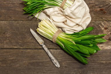 Taze bahar hasadı Ramson veya yaban pırasası demetleri. Eski ahşap masa arkasında mis kokulu yapraklar, sert ışık, karanlık gölge, kopyalama alanı