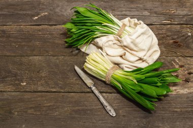 Taze bahar hasadı Ramson veya yaban pırasası demetleri. Eski ahşap masa arkasında mis kokulu yapraklar, sert ışık, karanlık gölge, kopyalama alanı