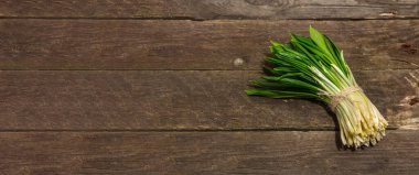 Taze bahar hasadı Ramson veya yaban pırasası. Eski ahşap masa zemininde mis kokulu yapraklar, sert ışık, koyu gölge, pankart biçimi