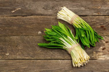 Taze bahar hasadı Ramson veya yaban pırasası demetleri. Eski ahşap masa arkasında mis kokulu yapraklar, sert ışık, karanlık gölge, kopyalama alanı