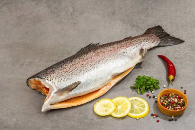 Gri taştan bir arka planda baharat ve bitkilerle çiğ alabalık leşi. Deniz balığı, sağlıklı yiyecek, yakın çekim.