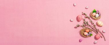 Geleneksel Paskalya kompozisyonu - yumurta, kuş yuvası, söğüt dalları, temalı dekor. Modern sert bir ışık, karanlık bir gölge, narin pembe bir arka plan.