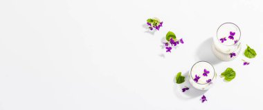 Taze menekşe çiçekli vegan panna cotta tatlısı. Çizgili renkli yiyecekler, modaya uygun stantlar. Sert bir ışık, koyu gölge, beyaz arkaplan, pankart biçimi