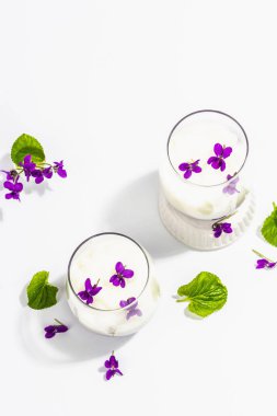 Taze menekşe çiçekli vegan panna cotta tatlısı. Çizgili renkli yiyecekler, modaya uygun stantlar. Sert bir ışık, koyu gölge, beyaz arkaplan, üst görünüm
