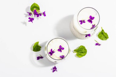 Taze menekşe çiçekli vegan panna cotta tatlısı. Çizgili renkli yiyecekler, modaya uygun stantlar. Sert bir ışık, koyu gölge, beyaz arkaplan, üst görünüm