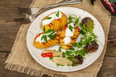 Pişmiş akordeon patatesler taze yeşillikler, mayalanmış sebzeler ve bezelye filizi. Geleneksel Amerikan yemekleri, ev yapımı vegan diyeti. Ahşap arkaplan, köy tarzı, kapat