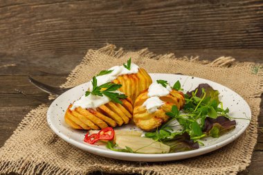 Pişmiş akordeon patatesler taze yeşillikler, mayalanmış sebzeler ve bezelye filizi. Geleneksel Amerikan yemekleri, ev yapımı vegan diyeti. Ahşap arkaplan, rustik biçim, kopyalama alanı