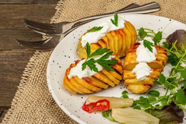 Pişmiş akordeon patatesler taze yeşillikler, mayalanmış sebzeler ve bezelye filizi. Geleneksel Amerikan yemekleri, ev yapımı vegan diyeti. Ahşap arkaplan, köy tarzı, kapat