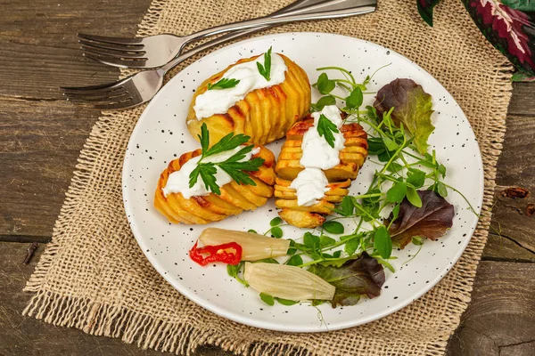 Pişmiş akordeon patatesler taze yeşillikler, mayalanmış sebzeler ve bezelye filizi. Geleneksel Amerikan yemekleri, ev yapımı vegan diyeti. Ahşap arkaplan, köy tarzı, kapat