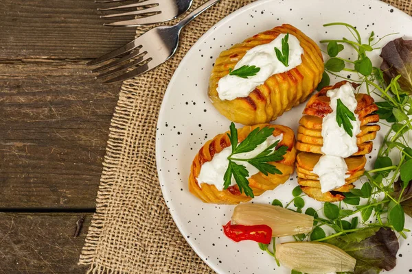 Pişmiş akordeon patatesler taze yeşillikler, mayalanmış sebzeler ve bezelye filizi. Geleneksel Amerikan yemekleri, ev yapımı vegan diyeti. Ahşap arkaplan, köy tarzı, üst görünüm