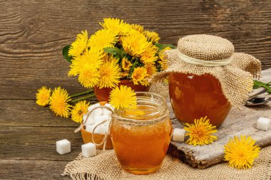 Dandelion jam or honey in the glass jar with a bouquet of fresh blooming dandelion flowers. Seasonal product, rustic style, wooden background, close up