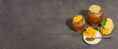 Karahindiba reçeli ya da cam kavanozda taze karahindiba çiçekleri olan bal. Mevsimlik ürün, modaya uygun sert ışık, karanlık gölge. Taş beton arkaplan, pankart biçimi