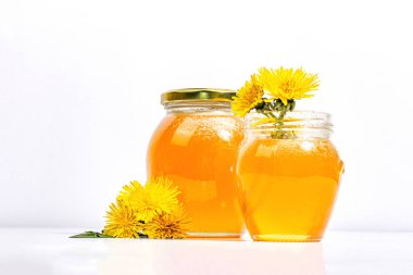 Karahindiba reçeli ya da cam kavanozda bal ve beyaz arka planda taze karahindiba çiçekleri. Mevsimlik ürün, modaya uygun sert ışık, karanlık gölge, kopyalama alanı