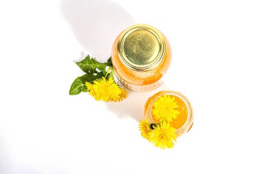 Dandelion jam or honey in the glass jar with fresh dandelion flowers isolated on white background. Seasonal product, trendy hard light, dark shadow, top view