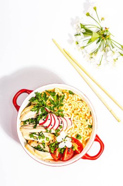 Tavuk, sebze ve otlu Asya erişteleri beyaz arka planda izole edilir. Geleneksel Japon çorbası, çorba ve kiraz çiçekleri, üst manzara.