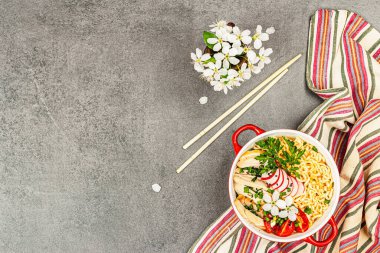 Kırmızı bir kasede tavuk, sebze ve otlu Asya eriştesi. Geleneksel Japon çorbası, çorba ve kiraz çiçekleri. Gri taş arkaplan, üst manzara