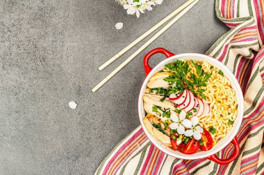 Kırmızı bir kasede tavuk, sebze ve otlu Asya eriştesi. Geleneksel Japon çorbası, çorba ve kiraz çiçekleri. Gri taş arkaplan, üst manzara