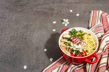 Kırmızı bir kasede tavuk, sebze ve otlu Asya eriştesi. Geleneksel Japon çorbası, çorba ve kiraz çiçekleri. Taş beton zemin, modaya uygun sert ışık, karanlık gölge, kopyalama alanı