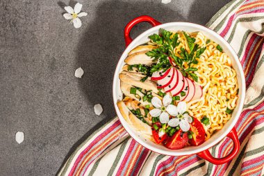 Kırmızı bir kasede tavuk, sebze ve otlu Asya eriştesi. Geleneksel Japon çorbası, çorba ve kiraz çiçekleri. Taş beton arka plan, modaya uygun sert ışık, koyu gölge, üst manzara