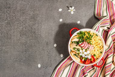 Kırmızı bir kasede tavuk, sebze ve otlu Asya eriştesi. Geleneksel Japon çorbası, çorba ve kiraz çiçekleri. Taş beton arka plan, modaya uygun sert ışık, koyu gölge, üst manzara