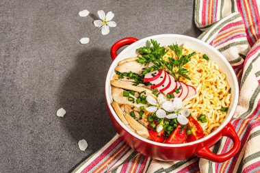 Kırmızı bir kasede tavuk, sebze ve otlu Asya eriştesi. Geleneksel Japon çorbası, çorba ve kiraz çiçekleri. Taş beton zemin, modaya uygun sert ışık, karanlık gölge, kopyalama alanı