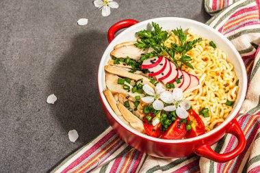 Kırmızı bir kasede tavuk, sebze ve otlu Asya eriştesi. Geleneksel Japon çorbası, çorba ve kiraz çiçekleri. Taş beton zemin, modaya uygun sert ışık, karanlık gölge, kopyalama alanı