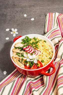 Kırmızı bir kasede tavuk, sebze ve otlu Asya eriştesi. Geleneksel Japon çorbası, çorba ve kiraz çiçekleri. Taş beton arka plan, modaya uygun sert ışık, karanlık gölge, kapat