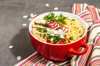 Kırmızı bir kasede tavuk, sebze ve otlu Asya eriştesi. Geleneksel Japon çorbası, çorba ve kiraz çiçekleri. Taş beton zemin, modaya uygun sert ışık, karanlık gölge, kopyalama alanı