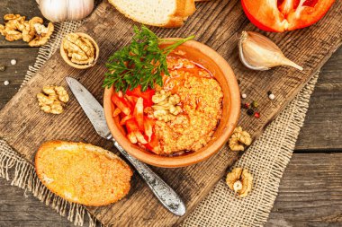 Geleneksel Ortadoğu sosu Muhammara. Ceviz ve baharatlı kavrulmuş kırmızı dolma biber. Seramik bir kasede düz ekmekle servis edilmiş, eski ahşap arka plan, üst manzara.