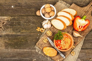 Geleneksel Ortadoğu sosu Muhammara. Ceviz ve baharatlı kavrulmuş kırmızı dolma biber. Seramik bir kasede düz ekmekle servis edilmiş, eski ahşap arka plan, üst manzara.