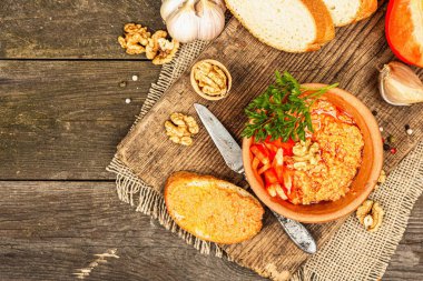Geleneksel Ortadoğu sosu Muhammara. Ceviz ve baharatlı kavrulmuş kırmızı dolma biber. Seramik bir kasede düz ekmekle servis edilmiş, eski ahşap arka plan, üst manzara.