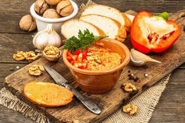 Geleneksel Ortadoğu sosu Muhammara. Ceviz ve baharatlı kavrulmuş kırmızı dolma biber. Seramik bir kasede düz ekmekle servis edilir, eski ahşap arka plan, kapat.