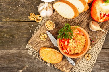 Geleneksel Ortadoğu sosu Muhammara. Ceviz ve baharatlı kavrulmuş kırmızı dolma biber. Seramik bir kasede düz ekmekle servis edilmiş, eski ahşap arka plan, üst manzara.