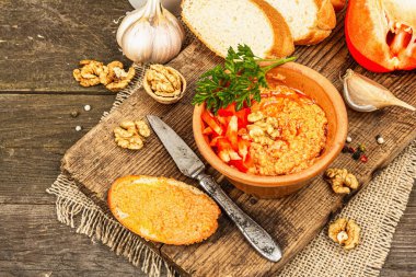 Geleneksel Ortadoğu sosu Muhammara. Ceviz ve baharatlı kavrulmuş kırmızı dolma biber. Seramik bir kasede düz ekmekle servis edilir, eski ahşap arka plan, kapat.