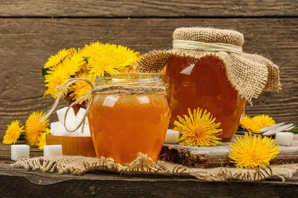 Dandelion jam or honey in the glass jar with a bouquet of fresh blooming dandelion flowers. Seasonal product, rustic style, wooden background, close up