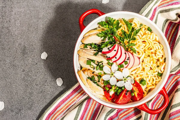 Kırmızı bir kasede tavuk, sebze ve otlu Asya eriştesi. Geleneksel Japon çorbası, çorba ve kiraz çiçekleri. Taş beton arka plan, modaya uygun sert ışık, koyu gölge, üst manzara