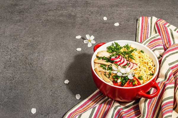 Kırmızı bir kasede tavuk, sebze ve otlu Asya eriştesi. Geleneksel Japon çorbası, çorba ve kiraz çiçekleri. Taş beton zemin, modaya uygun sert ışık, karanlık gölge, kopyalama alanı