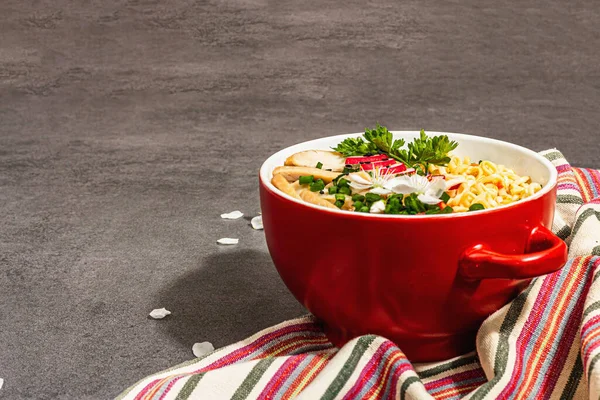 Kırmızı bir kasede tavuk, sebze ve otlu Asya eriştesi. Geleneksel Japon çorbası, çorba ve kiraz çiçekleri. Taş beton zemin, modaya uygun sert ışık, karanlık gölge, kopyalama alanı