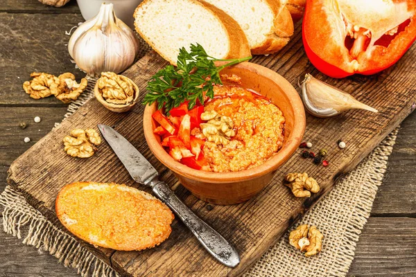 Geleneksel Ortadoğu sosu Muhammara. Ceviz ve baharatlı kavrulmuş kırmızı dolma biber. Seramik bir kasede düz ekmekle servis edilir, eski ahşap arka plan, kapat.