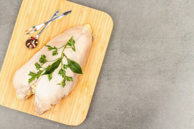 Baharatlı çiğ tavuk göğsü ve taze maydanoz. Çiftlik ürünleri, BIO kümes hayvanları. Sağlıklı gıda konsepti, modaya uygun sert ışık, karanlık gölge. Gri beton zemin, üst manzara