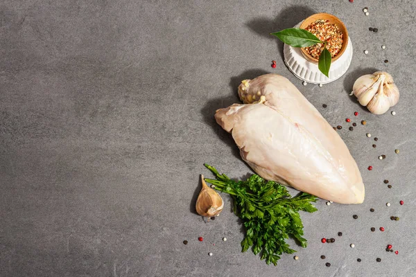 Raw chicken breast with spices and fresh parsley. Farm product, BIO poultry. Healthy food concept, trendy hard light, dark shadow. Grey concrete stone background, top view