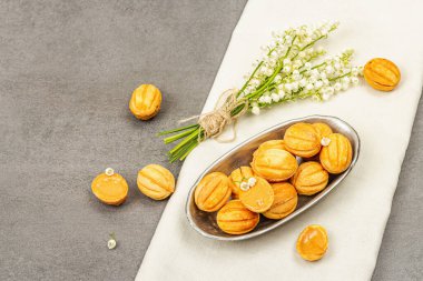 Yoğunlaştırılmış süt kremalı ceviz şeklinde kurabiyeler. Lezzetli kurabiyeli sandviçler, Lily Valley buket desenli modern vejetaryen pişirme. Taş beton arkaplan, kopyalama alanı