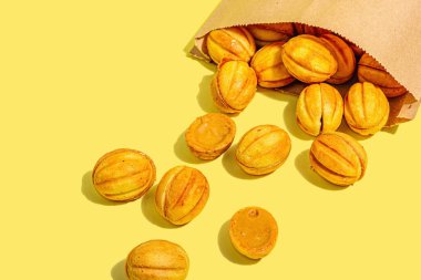 Yoğunlaştırılmış süt kremalı ceviz şeklinde kurabiyeler. Lezzetli sandviçler, modern vejetaryen pişirme. Moda sabit ışık, koyu gölge, sarı arkaplan, kopyalama alanı